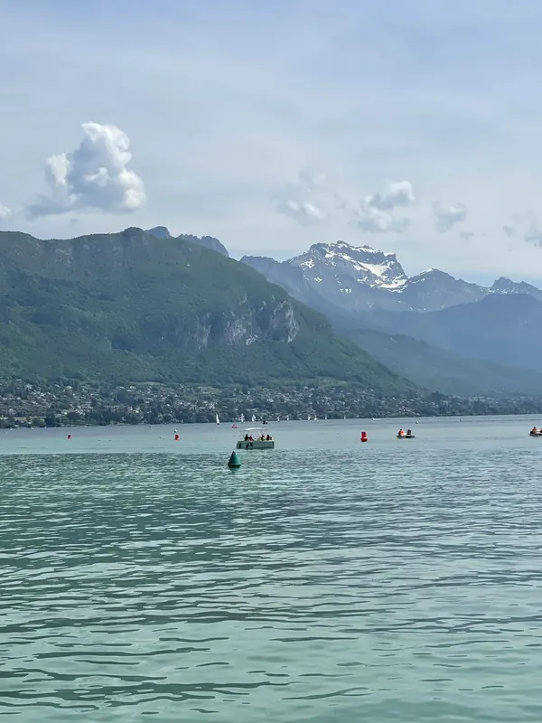 Turquoise water of Lake Annecy with forested mountains and snow-capped peaks behind