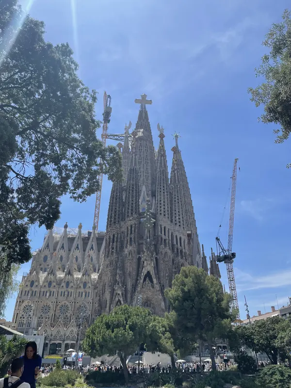 The spires of the Sagrada Família rising above trees under a bright blue sky