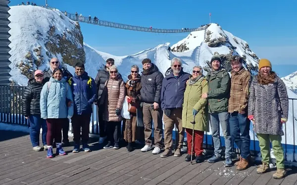 A group of people in winter coats on a viewing deck, with the Peak Walk bridge and snowy peaks behind