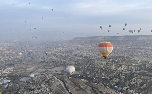 Hot-air balloons floating above the eroded valleys of Cappadocia, seen from another balloon
