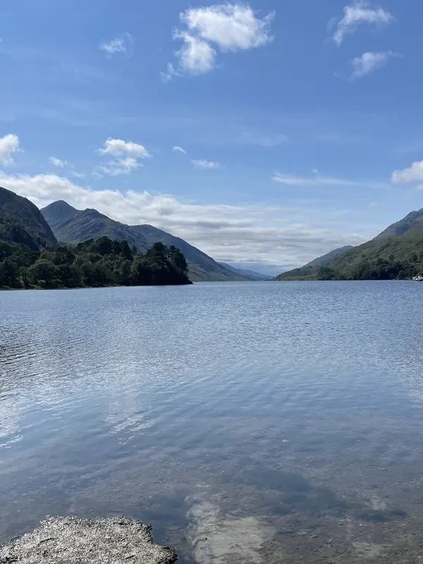 The still water of Loch Shiel stretching between steep green mountains under scattered clouds