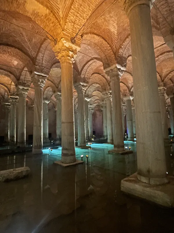 Rows of marble columns rising from still water under brick vaults in the Basilica Cistern, lit in warm amber