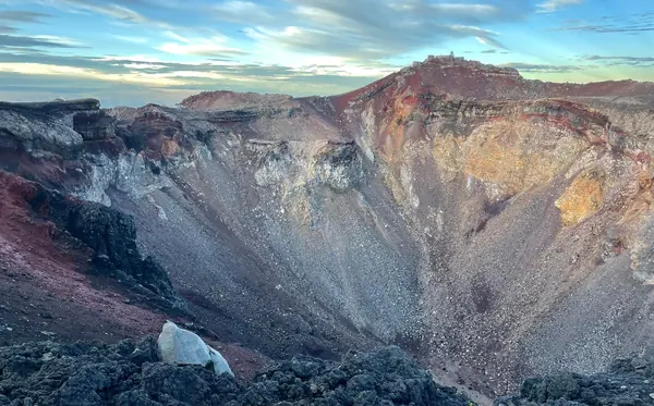 The vast red and grey crater at the summit of Mt Fuji under a streaked morning sky