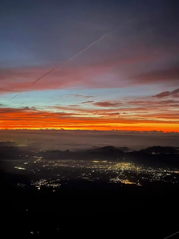 An orange dawn breaking above the clouds, with town lights twinkling far below