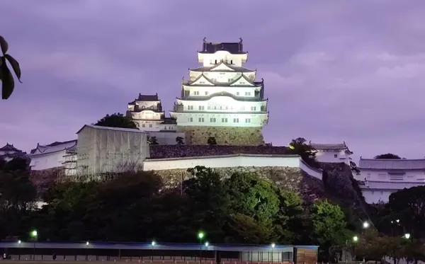 The white keep of Himeji Castle lit up on its stone walls under a purple evening sky