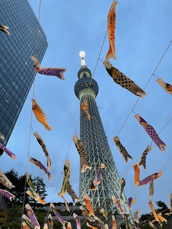 Tokyo Skytree rising behind rows of colourful koinobori carp streamers against a blue sky