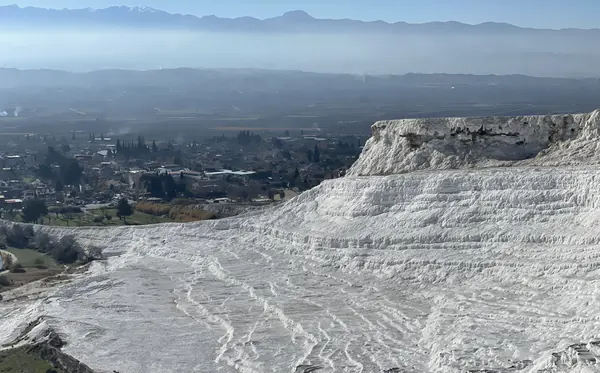 The white travertine terraces of Pamukkale cascading down towards the town, with the valley and snowy mountains beyond