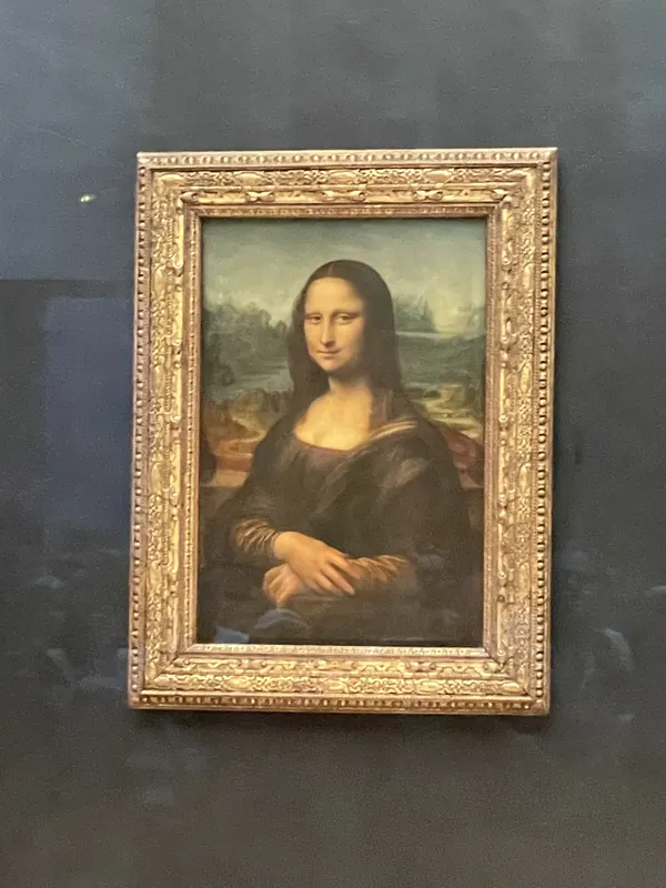 Leonardo da Vinci’s Mona Lisa in its gilded frame on a dark wall at the Louvre