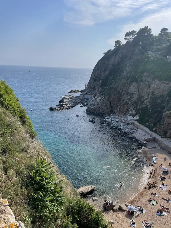 A small sandy cove with turquoise water below wooded cliffs at Tossa de Mar