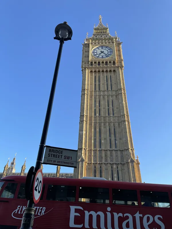 The Elizabeth Tower against a clear blue sky, with a red London bus passing below