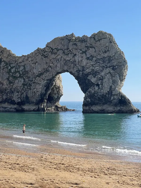 The great limestone arch of Durdle Door rising from turquoise sea, seen from the sandy beach