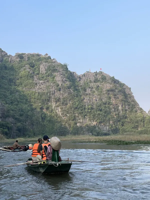 A rower guiding a small boat along a river beneath green karst cliffs