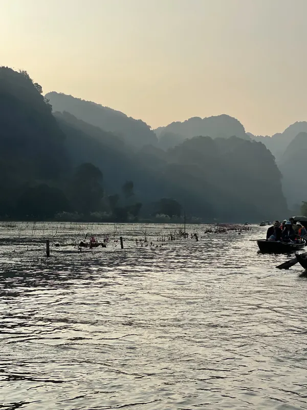 Layers of karst peaks fading into golden evening haze above a river with small boats